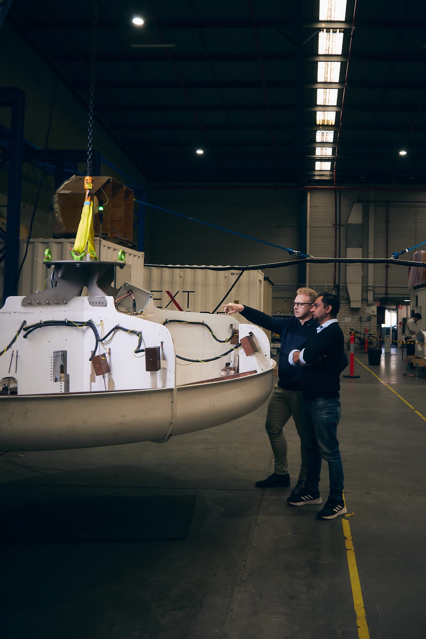 An ore sorting analyser on a hoist, two people gauging its scale alongside