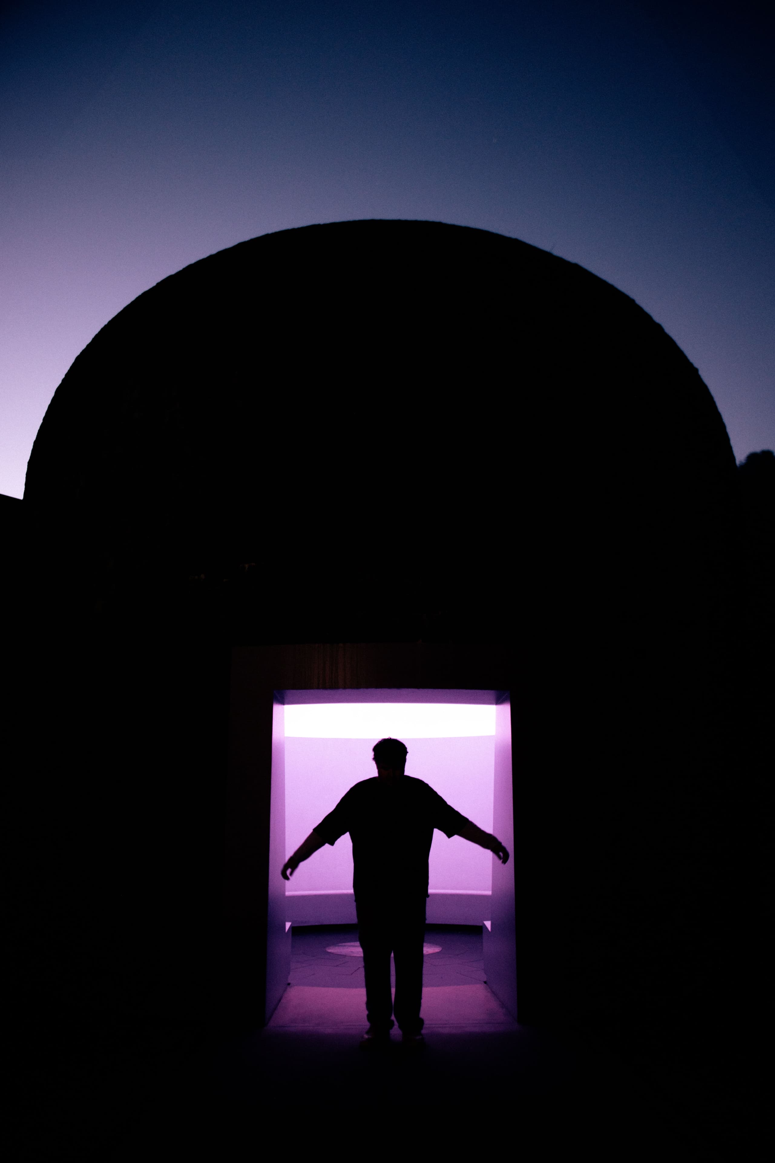 The dome silhouetted at dusk, a figure standing arms out in the lit entrance