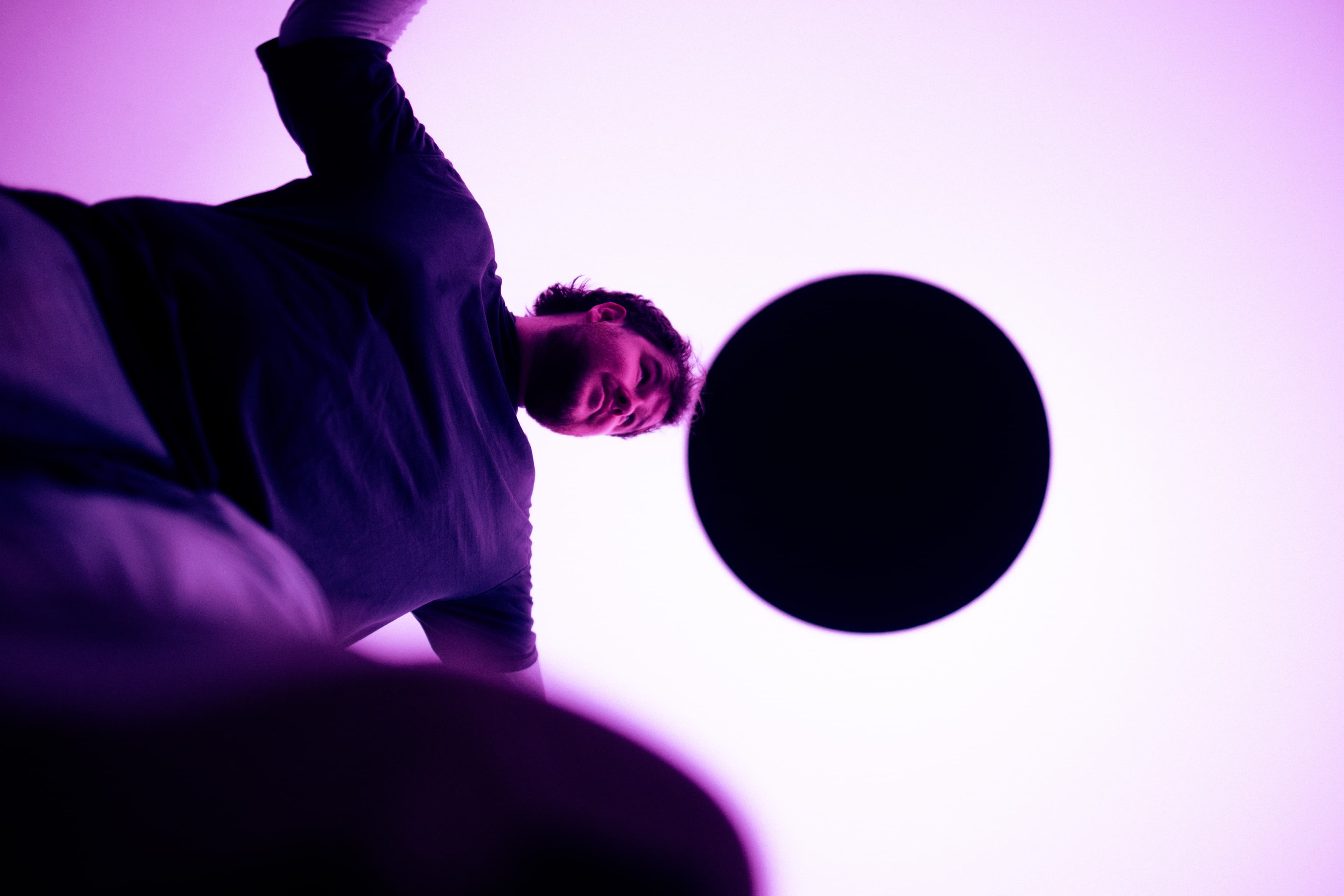 Magenta-lit portrait turned on its side, a black circular oculus alongside