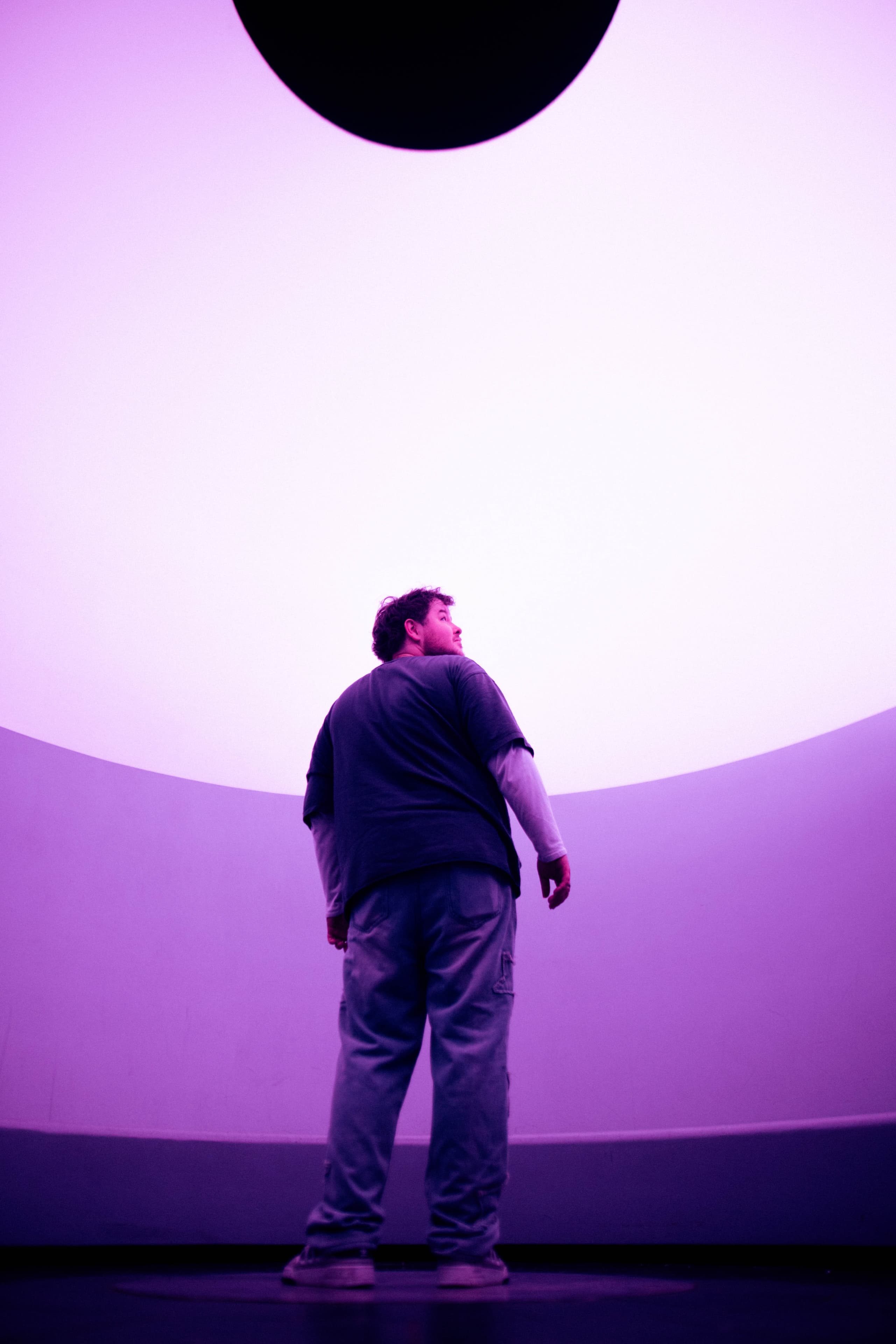 A person standing inside a magenta-lit dome, looking up toward the oculus