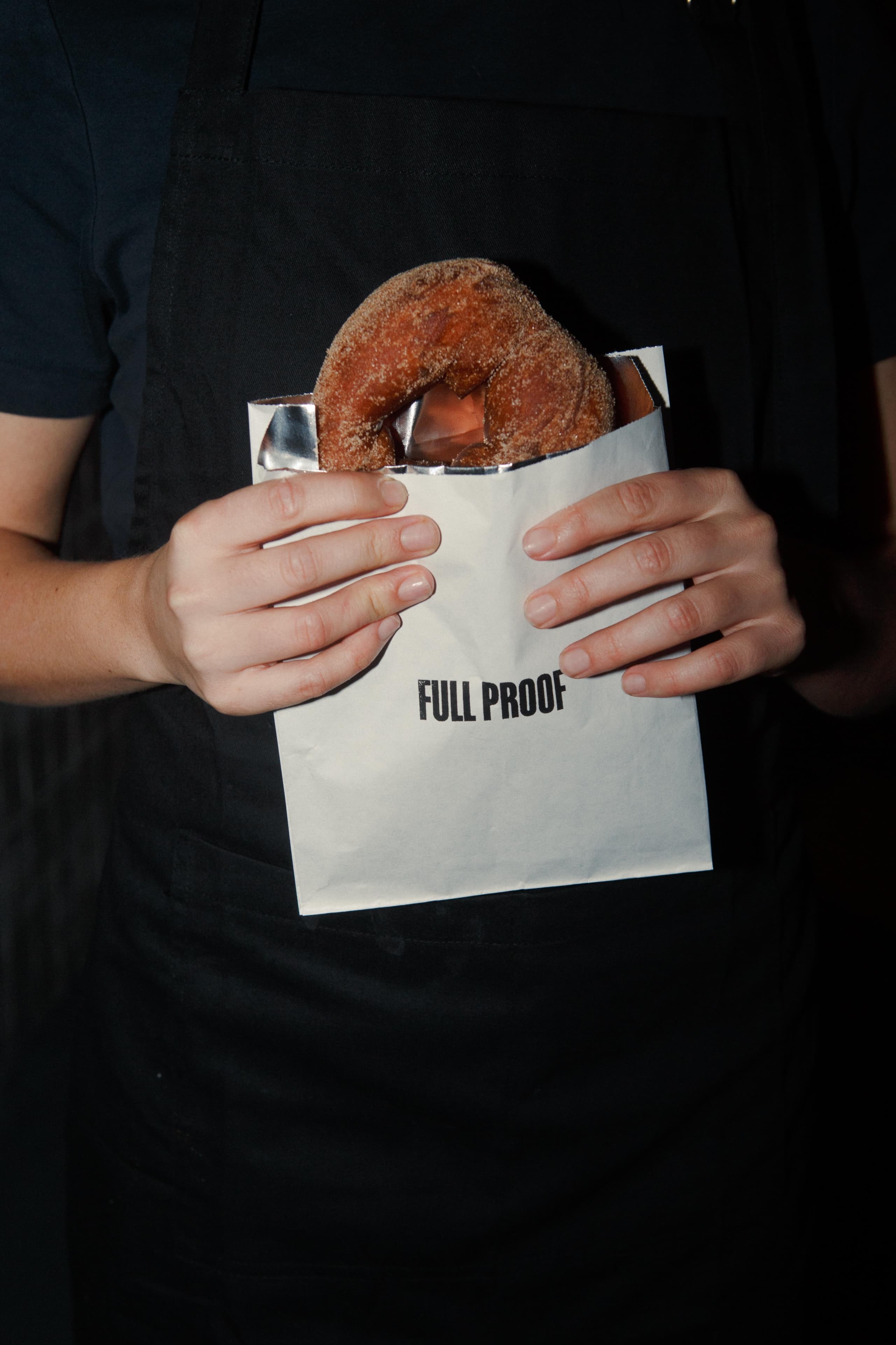 Close-up of hands holding Full Proof branded packaging showing the logo — hospitality brand identity and packaging design by Mude Sydney
